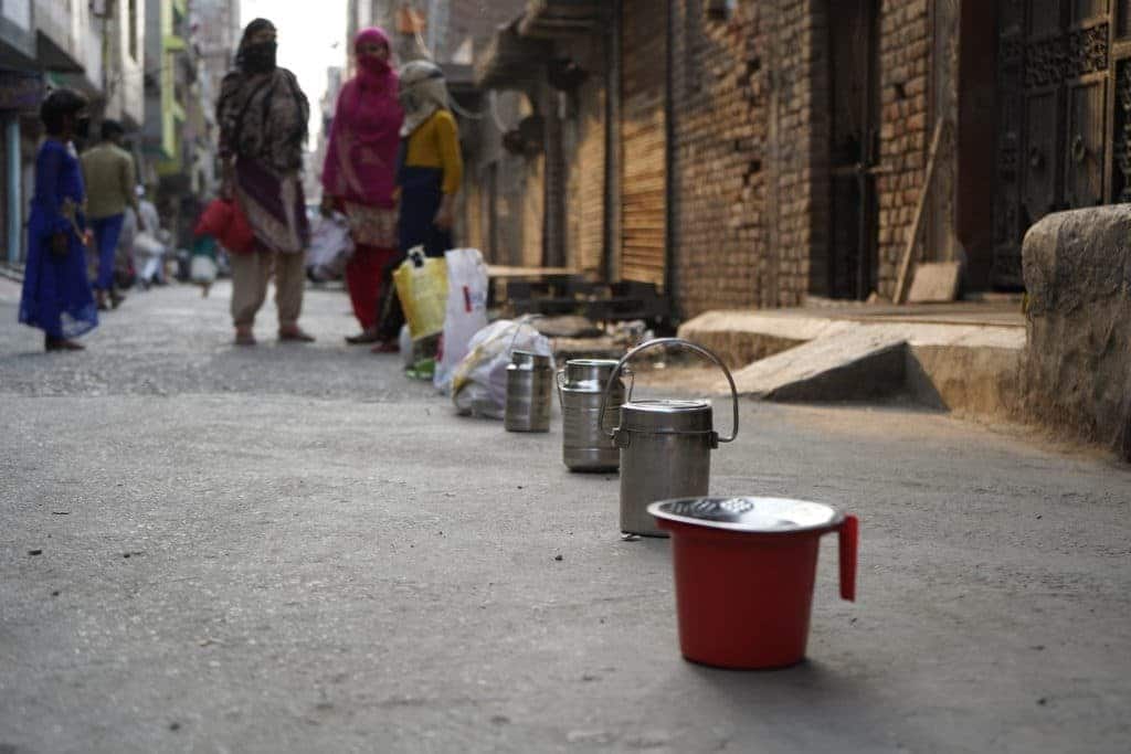 Women keeps tiffin boxes to hold their place in a line for ration food from NGO's in North-East Delhi